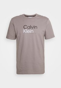 Gray cotton t-shirt with a crew neck, short sleeves, and a large "Calvin Klein" logo printed in black and white across the chest.