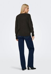 Mørkebrun strikket genser med avslappet passform, kombinert med mørkeblå jeans med rette ben. Modellen har på seg svarte hæler med et enkelt design.