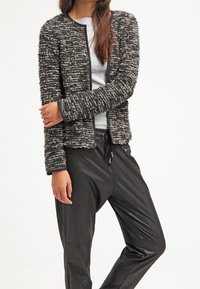 Svart och grå strukturerad stickad jacka med långa ärmar, rund halsringning och öppen fram; matchad med svarta glänsande tapered byxor.