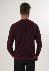 Burgunderfarbener, leichter Pullover mit gerippten Bündchen und Saum, der ein einfaches, strukturiertes Finish und Raglanärmel für optimale Bewegungsfreiheit bietet.