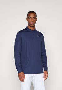 Marineblå långärmad polo med krage, med en vit Nike-logotyp på vänster bröst. Slät, lättviktsmaterial och klassisk passform.