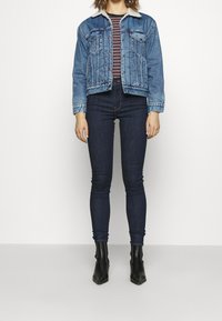 Ljusblå denimjacka med en vit syntetpälskrage, kombinerad med en randig topp och mörka skinnyjeans, bärs med svarta spetsiga ankelstövlar.