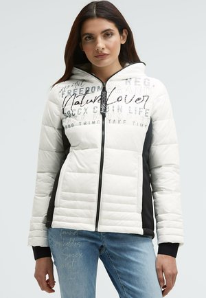 Weiße und schwarze gepolsterte Jacke mit Kapuze, mit bedrucktem Text und geometrischen Nähten, Reißverschluss und elastischen Bündchen. Jeans aus Denim.