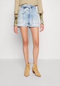Světle modré denimové šortky s páskem na uvázání, mají přední kapsy, uvolněný střih a nedokončený lem. Kombinované s tanovými semišovými kotníkovými botami.