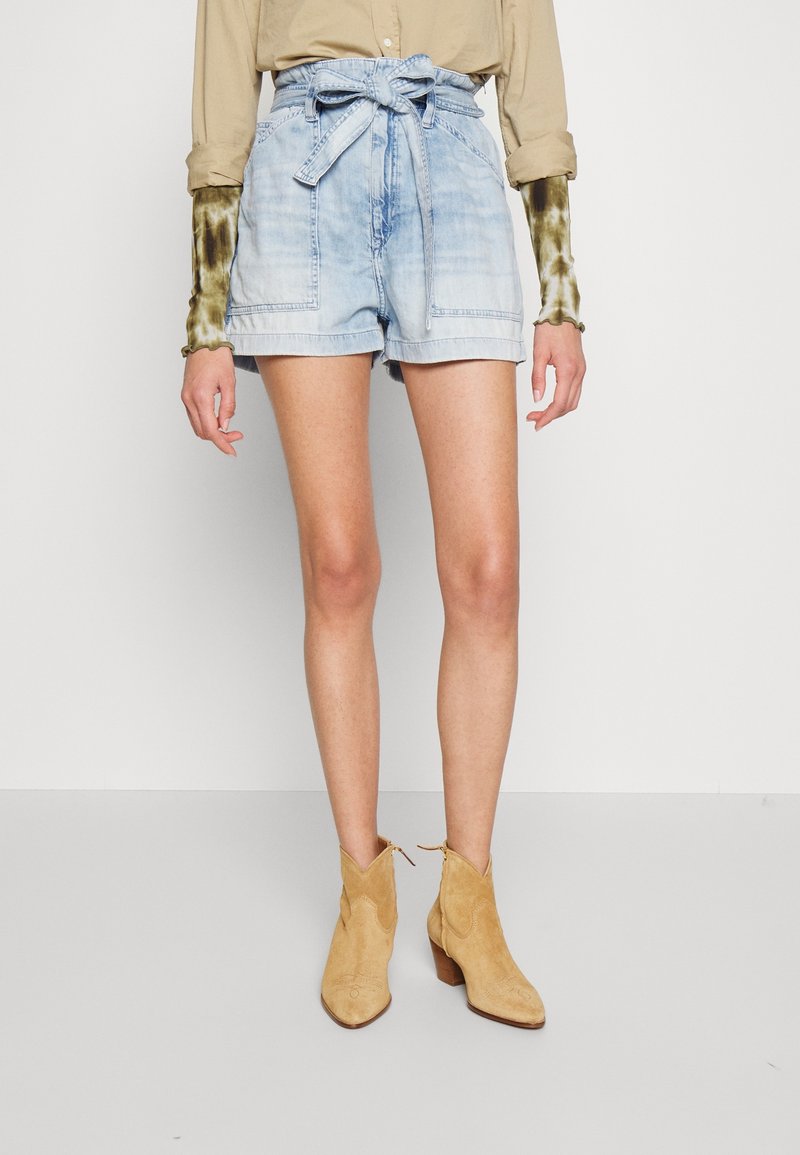 Světle modré denimové šortky s páskem na uvázání, mají přední kapsy, uvolněný střih a nedokončený lem. Kombinované s tanovými semišovými kotníkovými botami.