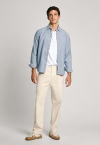 Lichtblauw overhemd over een witte t-shirt, gecombineerd met crèmekleurige broeken en casual sneakers. Glad materiaal en een ontspannen pasvorm.