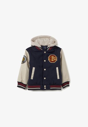 Donkerblauwe varsityjack met een crèmekleurige capuchon, rood-witte gestreepte accenten, geborduurd logo en twee voorzakken. Zachte stof textuur.