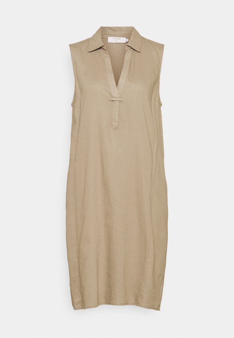 Robe beige sans manches longueur genou avec col et décolleté en V comportant un petit détail de sangle horizontale sous le décolleté.