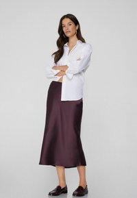 Biała koszula z guzikami, z podwiniętymi rękawami, zestawiona z ciemnofioletową satynową spódnicą midi. W komplecie z bordowymi butami wsuwanymi. Prosty, elegancki design.