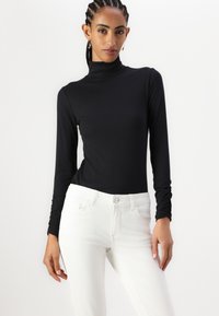 Maglione a collo alto a coste nere e jeans bianchi. Il maglione presenta maniche lunghe e una vestibilità aderente, mentre i jeans hanno un classico stile a cinque tasche.