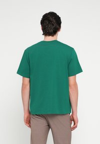 Zelené tričko s krátkými rukávy z měkké látky, s kulatým výstřihem a volným střihem. Bez viditelných vzorů nebo akcentů, jednoduchý design.