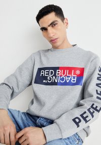 Sivi dukserica dugih rukava s šarenim grafičkim logotipom u crvenoj, plavoj i bijeloj boji. Natpis na rukavu glasi "PEPE JEANS."