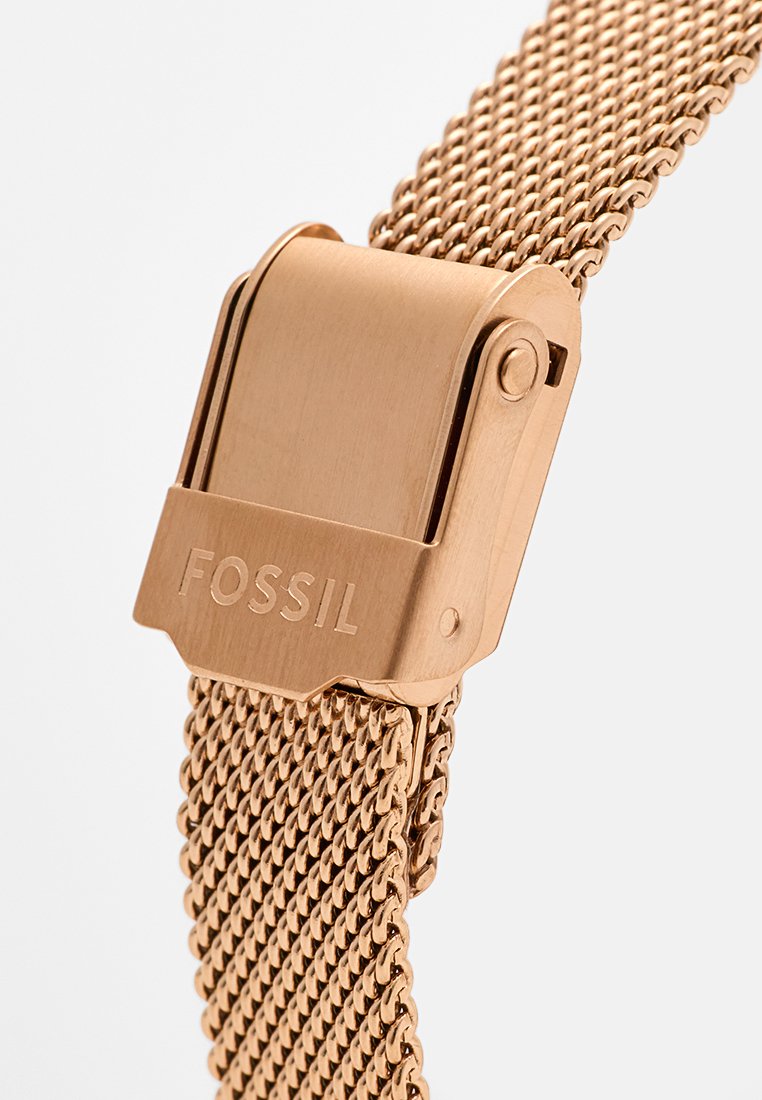 Armband aus roségoldfarbenem Netzgewebe mit einem metallischen Verschluss, auf dem die Marke "FOSSIL" eingraviert ist. Das Armband hat eine gewebte Textur und ein flexibles Design.