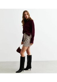 Bordeaux gebreid sweater, geruite mini rok, zwarte kniehoge laarzen met puntige neuzen, en een kleine bordeaux handtas. Minimalistische achtergrond.