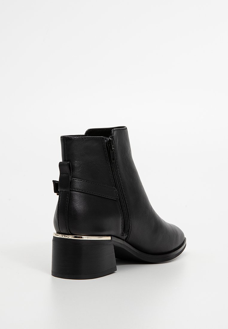 Bottine en cuir noir au design épuré, avec fermeture éclair sur le côté et un talon bloc avec accent métallique à la base.