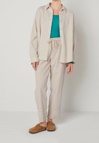 Beige corduroy shirt and pants set with a turquoise top underneath. Brown clogs, relaxed fit. Visually textured fabric and adjustable waistband.