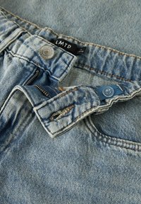 Svetloplave traperice s izblijedjelim uzorkom, s metalnim gumbom za zatvaranje, tkanom etiketom i patentnim zatvaračem. Naglašene kontrastnim šavovima.