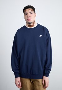 Sudadera azul marino con cuello redondo y mangas largas, que presenta un logo blanco de Nike en el pecho. Tejido suave; corte relajado.
