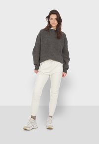 Szary krótki sweter z okrągłym dekoltem i obszerne rękawami, połączony z białymi spodniami tapered i jasnymi trampkami. Gładka tekstura całości.