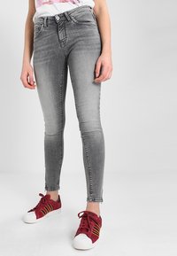 Jeans skinny grises con un patrón desgastado y sutiles arrugas, con una cintura alta, pasadores para cinturón y diseño de cinco bolsillos. Combinados con zapatillas rojas.