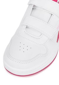 Zapatilla blanca de cuero con detalles rosas, que presenta tiras de Velcro, punta perforada para transpirabilidad y suela plana.