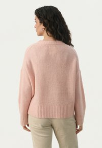 Un pull rose surdimensionné en tissu doux avec un ourlet et des poignets côtelés. Présente un col large et des épaules tombantes. Détails minimaux.