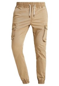 Beige cargobroek van zacht materiaal, met een elastische tailleband met trekkoord, taps toelopende enkels en meerdere zijzakken.