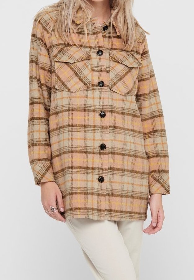Femme portant une chemise à manches longues à carreaux beige et marron avec deux poches poitrine, associée à un pantalon de couleur claire.
