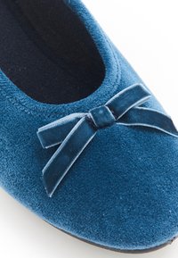 Bailarina de ante azul con punta redonda, con un lazo de terciopelo marino como acento y una superficie suave y texturizada. Forro interior negro visible.