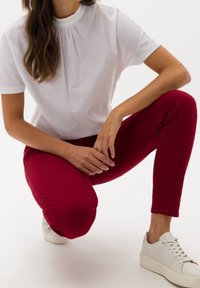 Top blanco de manga corta con un cuello alto, combinado con pantalones rojos ajustados y zapatillas blancas. Conjunto casual con texturas suaves.