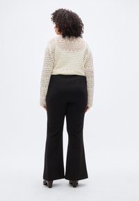 Κοντό πουλόβερ σε κρεμ απόχρωση με πλεχτό σχέδιο δαντέλας, σε συνδυασμό με μαύρο παντελόνι καμπάνα. Ορατή ραφή στη μέση και στα καμπανοειδή μπατζάκια.