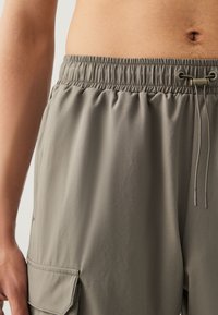 Shorts cargo gris en tissu léger, dotés d'une ceinture élastique avec cordon de serrage, de poches latérales et d'une texture lisse.