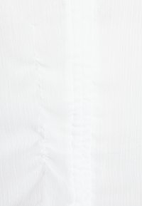 Tecido branco com uma textura estriada e costuras verticais, apresentando suaves pregas que criam profundidade e dimensão.