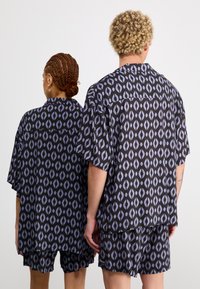 Camisas de manga corta impresas y pantalones cortos en negro con un patrón abstracto morado, presentando cortes sueltos y diseños relajados.