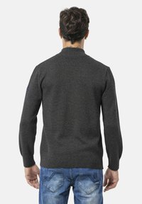 Grijze gebreide trui met een geribde kraag en mouwen, met een gladde textuur en een aansluitend ontwerp. Draagend met blauwe denim jeans.
