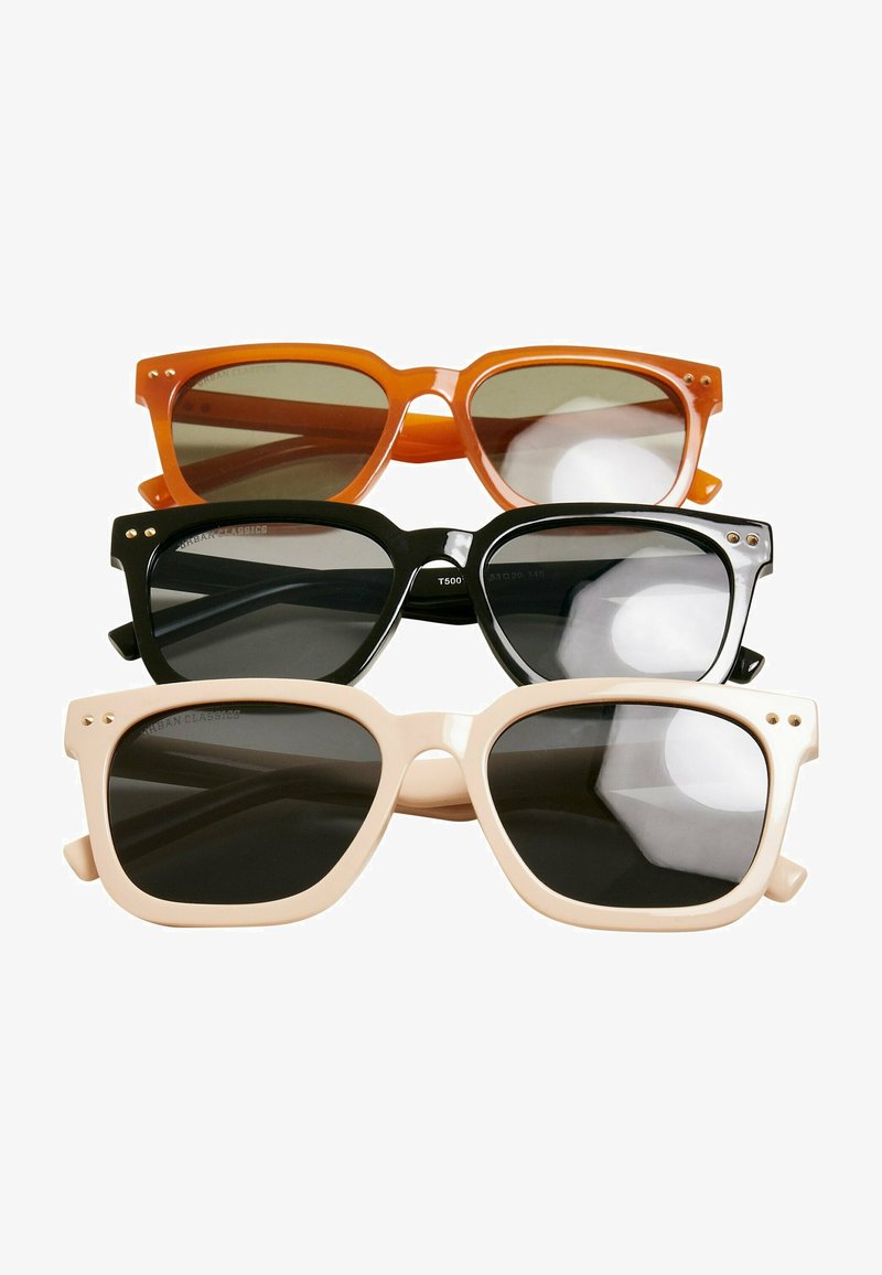 Trīs saulesbrilles: oranžas, melnas un krēma krāsas. Visām ir masīvas plastmasas ietvari, tumši objektīvi un zelta akcenti uz tempļiem.