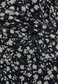 Svart tyg med små, vita blommönster som har klungor av blommor och spridda tunna linjer, visat med lätta veck och textur.