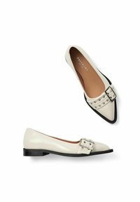 Chaussures plates en cuir verni crème avec un bout pointu, des accents noirs et un détail de boucle en argent à l'avant. Design à talon plat.