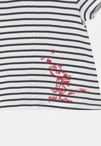 Pasiasta koszulka z krótkim rękawem w białym i granatowym kolorze, z czerwoną grafiką psa z sercami oraz wyhaftowanym napisem "petit bateau" poniżej.