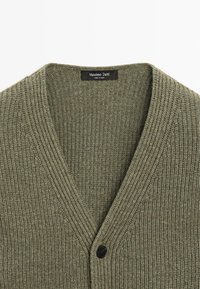 Cardigan in maglia a coste verde oliva con scollo a V e un solo bottone nero visibile, etichetta che riporta "Massimo Dutti Made in China".