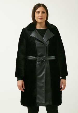 Manteau noir en tissu texturé et duveteux avec un devant en cuir lisse. Il comprend un col large, une ceinture à la taille et des manches longues.