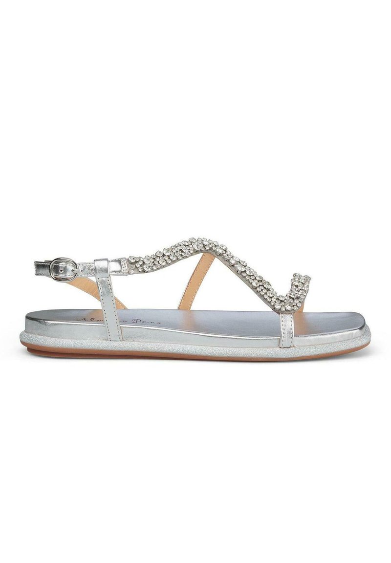 Sandalias plateadas con suela plana, que cuentan con una tira de joyas y hebilla ajustable en el tobillo. Acabado suave y diseño minimalista.