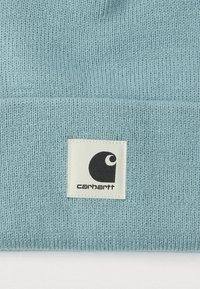 Ανοιχτό μπλε πλεκτό σκουφάκι από μαλακό υλικό. Διαθέτει τετράγωνο λευκό ταμπελάκι με μαύρο λογότυπο στο μπροστινό μέρος.