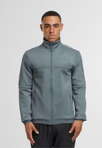 Szara kurtka sportowa z wysokim kołnierzem, zapięciem na zamek i kieszeniami bocznymi. Posiada teksturowane panele siateczkowe na rękawach dla lepszej wentylacji i dopasowania.