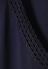 Tejido azul marino con una textura suave, que presenta un detalle trenzado a lo largo de un lado, añadiendo dimensionalidad y contraste al diseño.