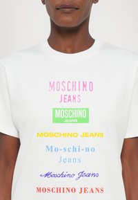 White cotton t-shirt featuring multiple colorful "Moschino Jeans" logos in various fonts and sizes, displayed in a vertical pattern.