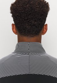 Zwart-wit gestreepte polo shirt met een hoge kraag, gestructureerde stof en een duidelijke scheiding van de strepen van het effen zwart aan de onderkant.