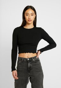Fekete bordázott hosszú ujjú crop top, csipkés szegéllyel. Magas derekú szürke farmernadrággal párosítva, gombos záródással és zsebekkel.
