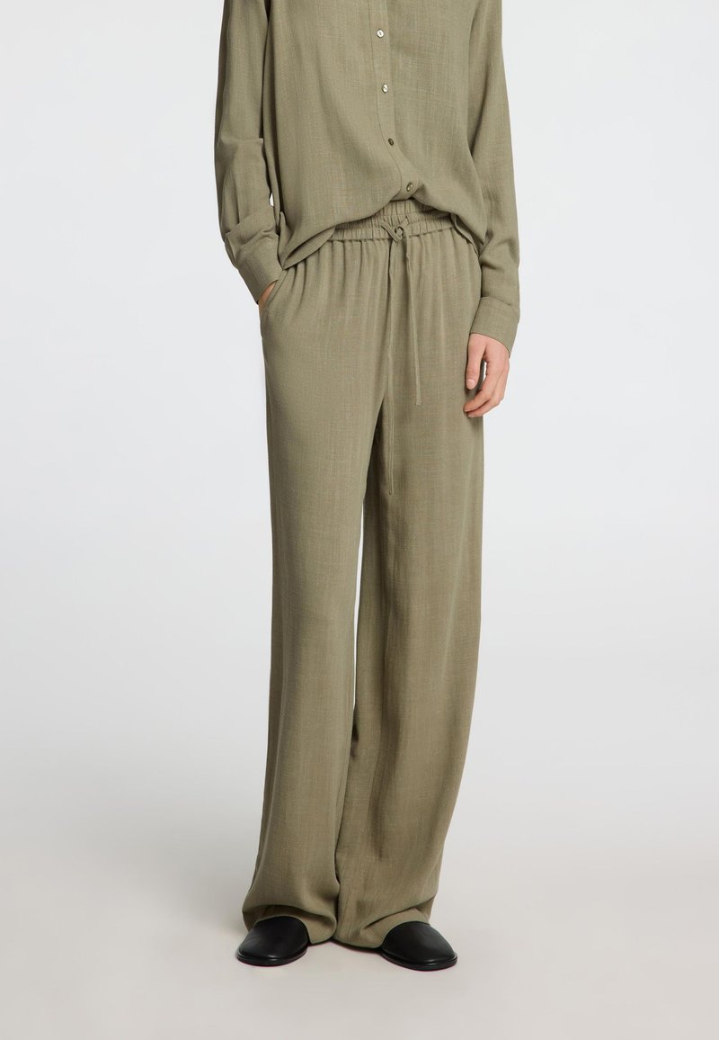 Pantalons légers de couleur vert olive, amples, avec une taille à cordon de serrage et des poches latérales, associés à une chemise à manches longues assortie.