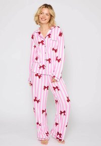 Conjunto de pijama a rayas rosas con patrones de lazo rojo, que incluye una parte superior abotonada con bolsillo y pantalones holgados. Tela suave y liviana.
